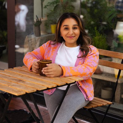 Shani Dhanda sitting at table with drink, outside