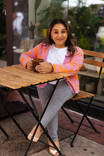 Shani Dhanda sitting at table with drink, outside